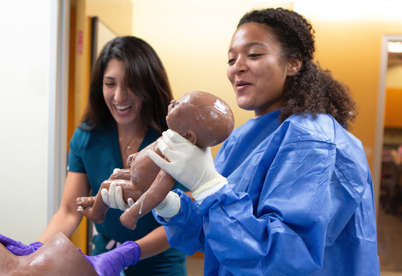 Smiling midwifery students deliver a 'simulated' baby during Midwifery Skills day.