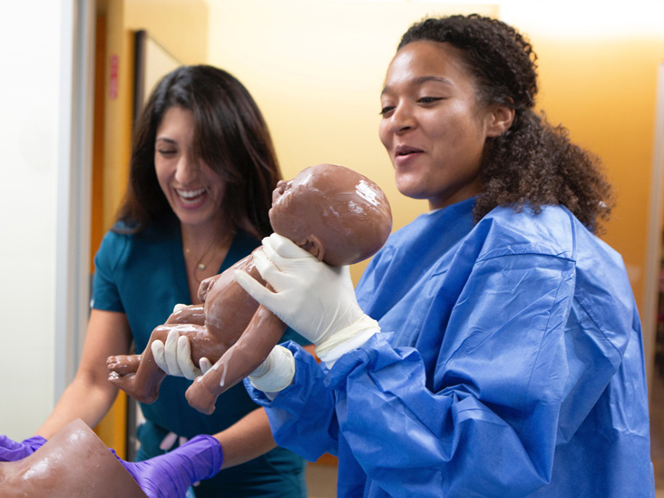 Smiling midwifery students deliver a 'simulated' baby during Midwifery Skills day.