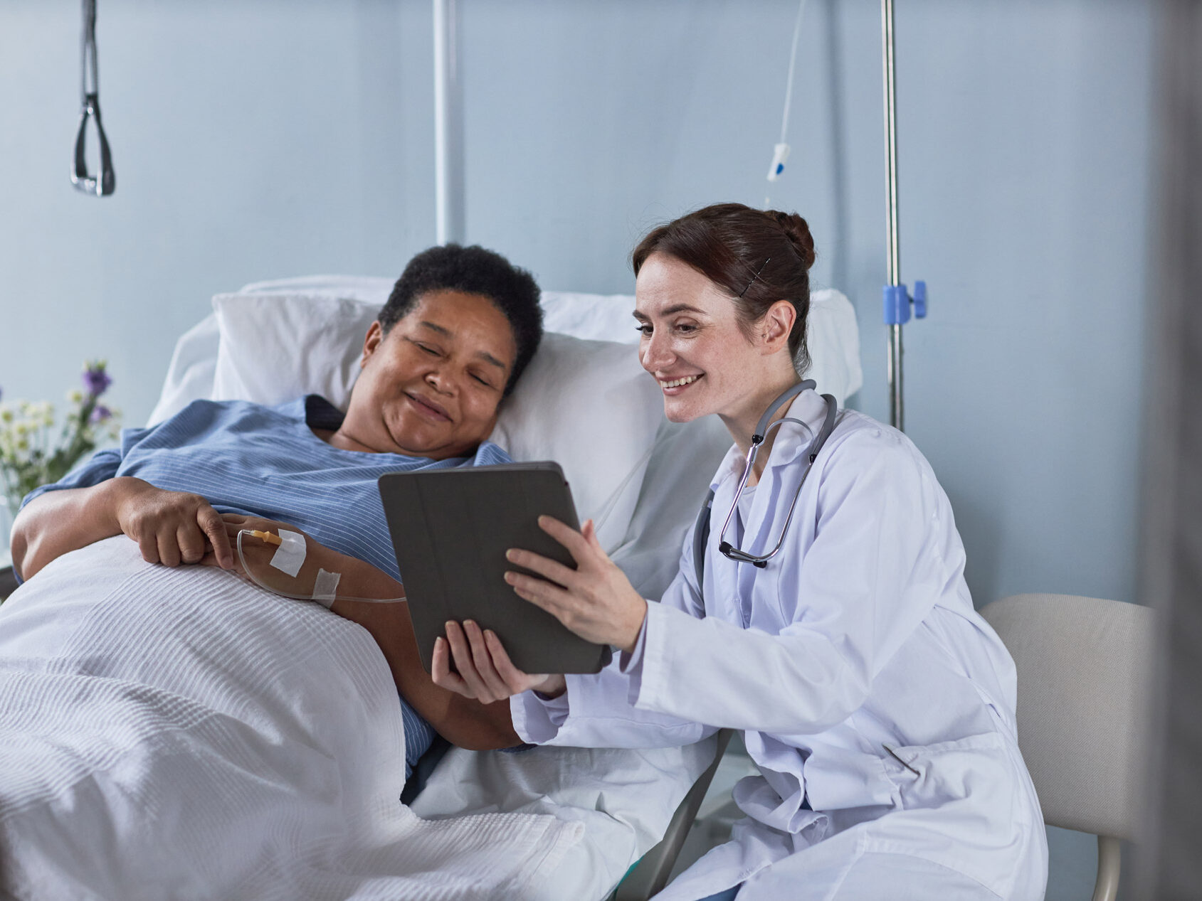 Nurse in White coat showing the patient a tablet, while smiling.