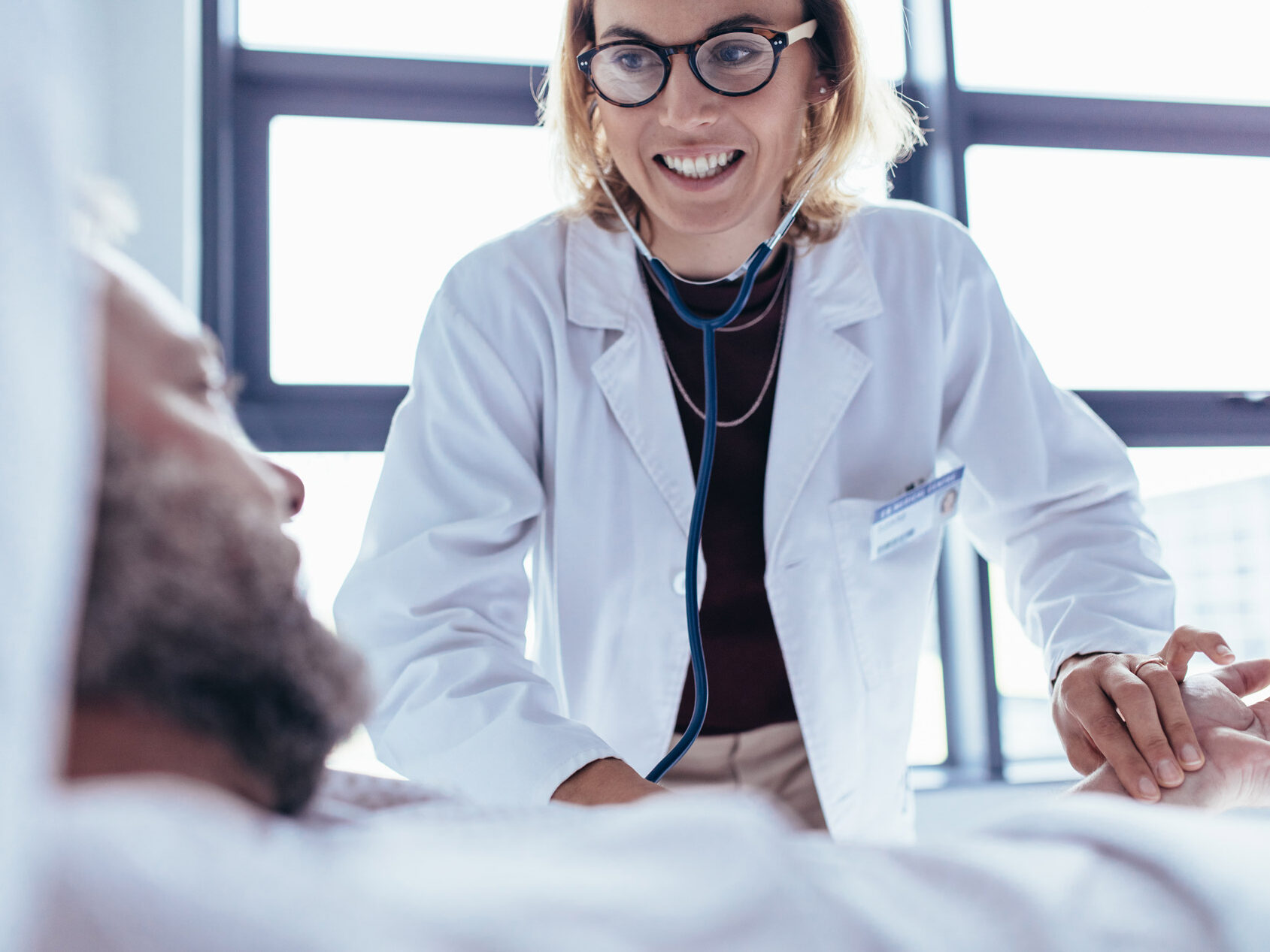 AGAC Nurse in White Coat smiling at patient who is lying in a hospital bed